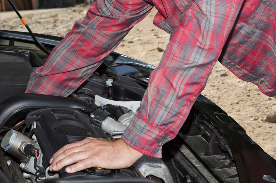 A man in a checked shirt opens the bonnet of a car and takes a look at the engine.