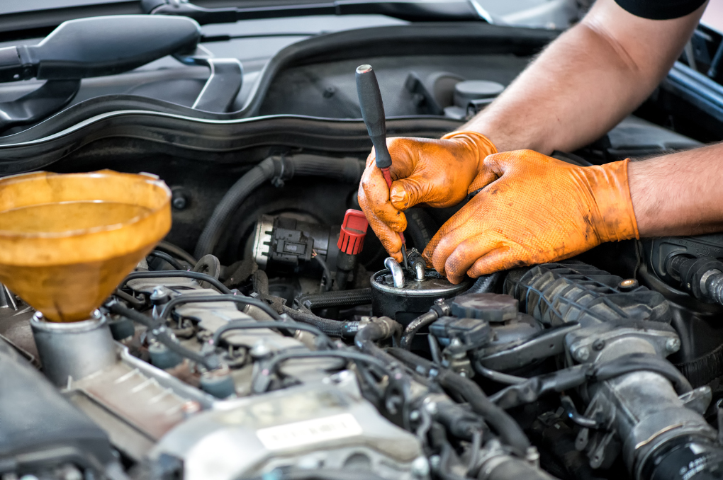 A mechanic wearing orange gloves covered in oil fixes a car's engine.