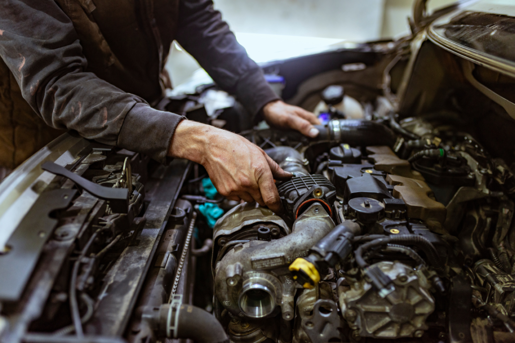 A mechanic fixes a car's engine with the hood up.